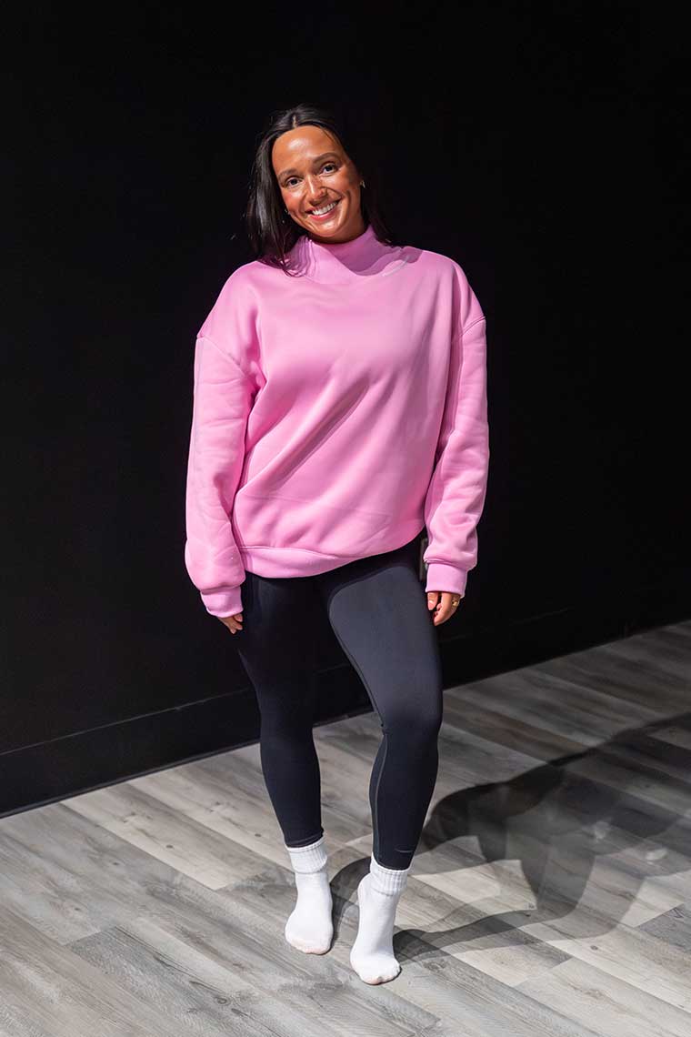 Person wearing a pink sweater and black leggings standing against a dark background