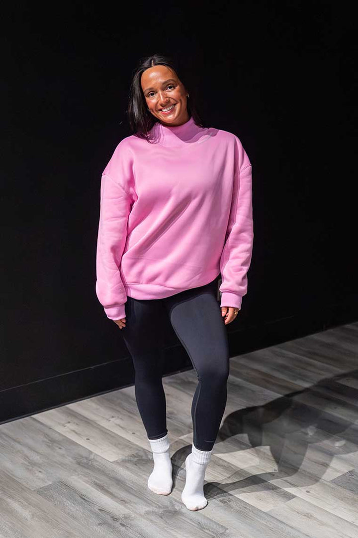 Person wearing a pink sweater and black leggings standing against a dark background